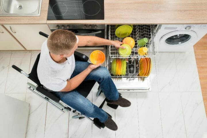 A man in a wheelchair using an accessible dishwasher