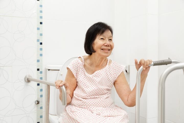 Senior woman holding on handrail in the toilet
