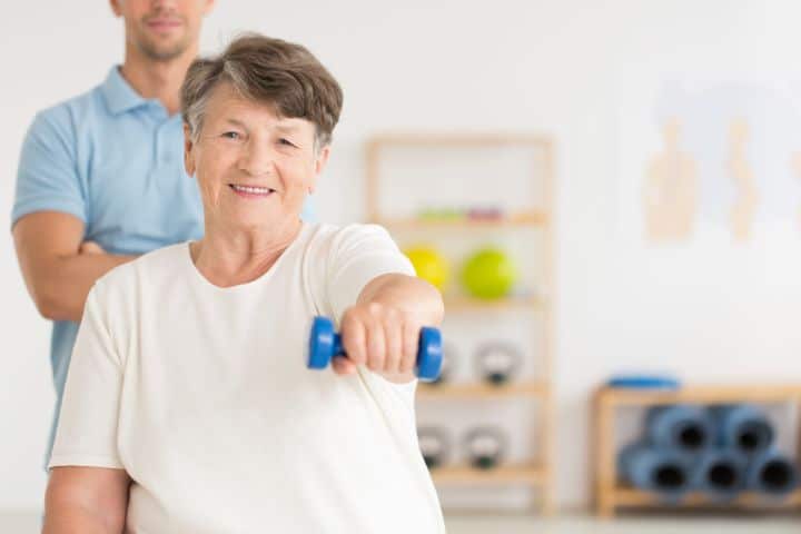 senior woman lifting dumbbell assisted by a physiotherapist