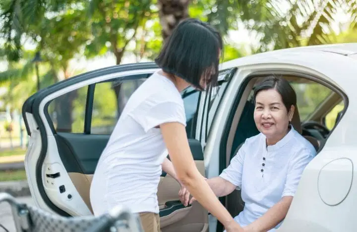 Woman helping Asian senior woman get into the car