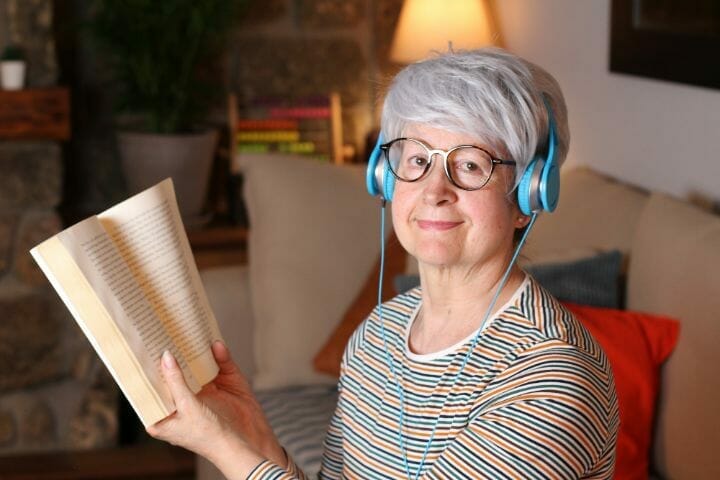 senior woman with headphone on while reading a book
